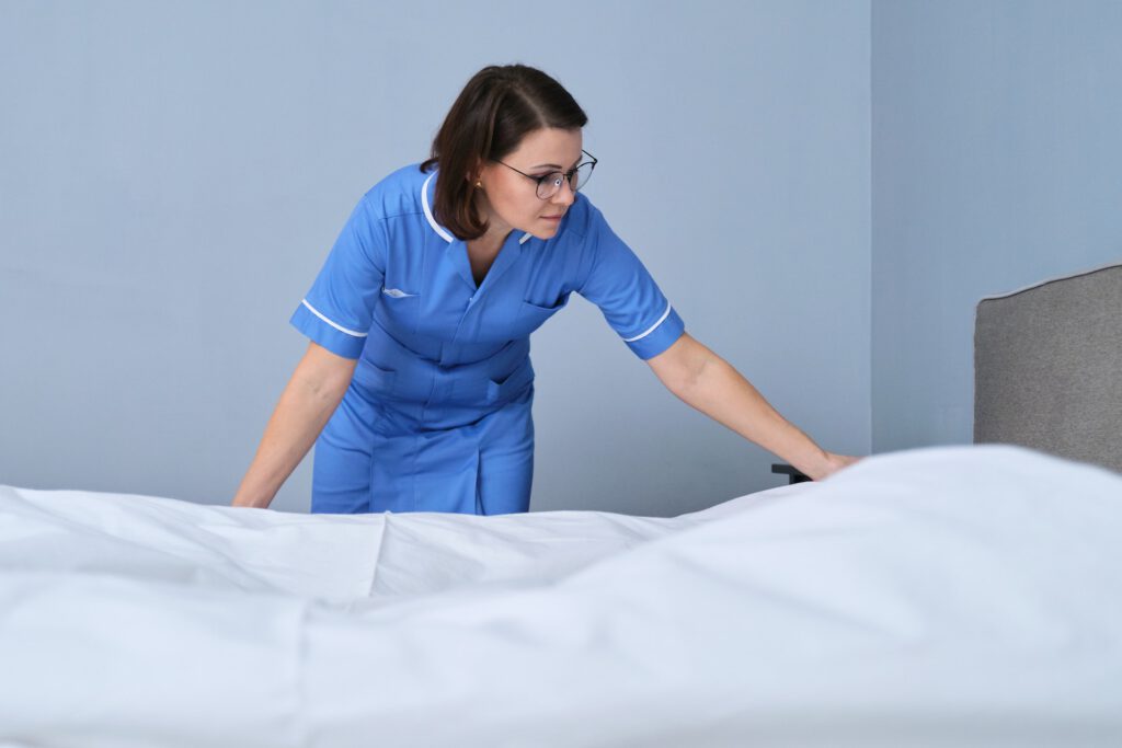 Middle aged female professional maid making bed in hotel room